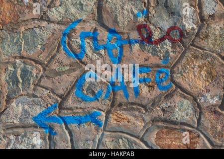 Stone wall outdoors, with a hand written 'cafe' in arabian and latin script and an arrow pointing out the direction. Stock Photo