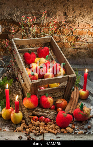 Christmas decoration, hand felted apples in wooden box, lit red candles, bark, spices and rose hips on wooden table in front of Stock Photo