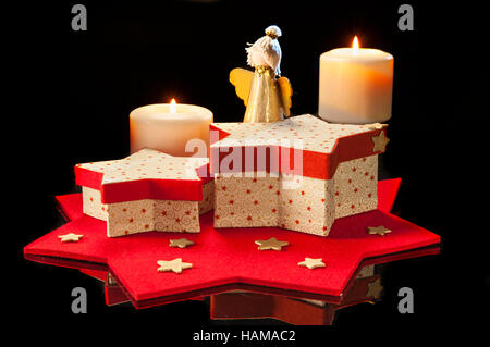 Christmas decoration, red and white star-shaped boxes, little golden angel, two lit candles, felted star, black background Stock Photo