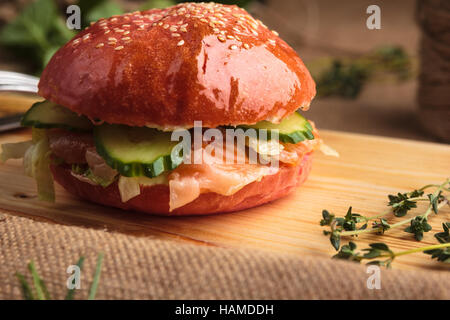 Concept: restaurant menus, healthy eating, homemade, gourmands, gluttony. Trendy glossy burger with salmon in pink bun with ingredients on messy vinta Stock Photo