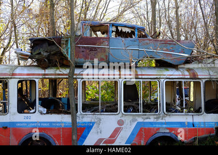 An old city bus is abandoned in a junkyard in Frankfort, Indiana with an old car sitting on top of it. Stock Photo