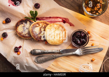 Concept: restaurant menus, healthy eating, homemade, gourmands, gluttony. Cheese pancakes with cherry sauce served on paper with ingredients on vintag Stock Photo