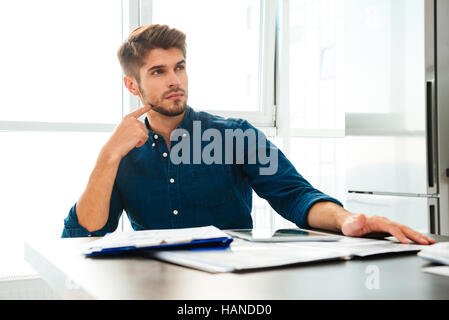Picture of concentrated young man at home thinking about finances. Look aside and touching his face. Stock Photo