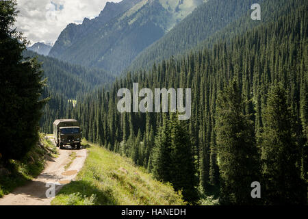 A military truck travels on an unpaved road through the valley full of conifers Stock Photo