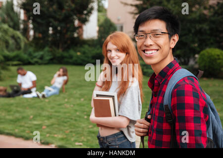Smiling asian young man student with backpack walking with her girlfriend outdoors Stock Photo