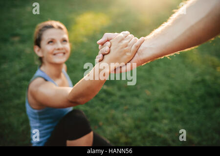 Close up shot of man helping woman to stand up. Focus on hands of couple exercising at park.