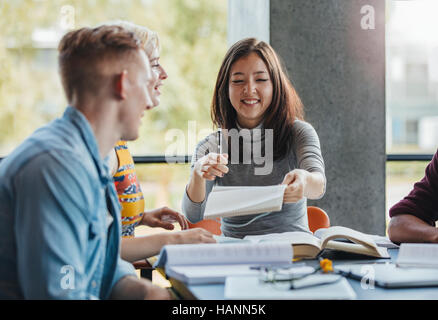 Young people sitting at table sharing notes for school assignment. Group of students studying together in a library. Stock Photo