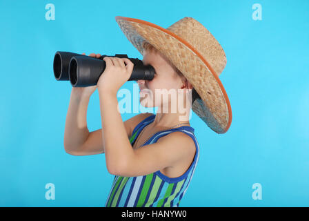 Curious boy in cowboy hat looking through binoculars. Photo on a blue background Stock Photo