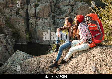 Adventure couple sitting on a rock. side view. couple looking away Stock Photo