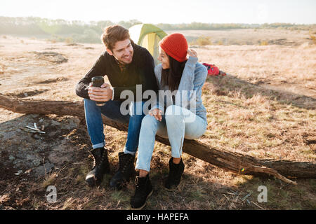 Couple near the tent. sitting on a log Stock Photo