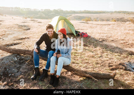 Young couple near the tent sitting on log. Stock Photo