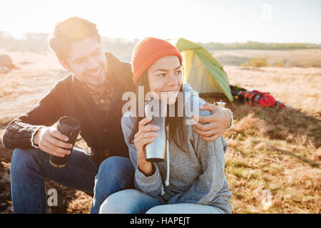 Happy couple with tea sitting on log near the tent Stock Photo