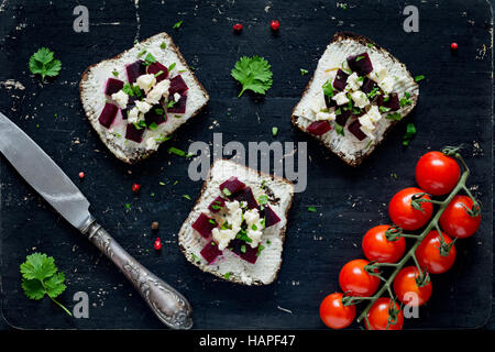 Goat cheese, roasted beet and feta cheese appetizer sandwiches on black cutting board, top view Stock Photo