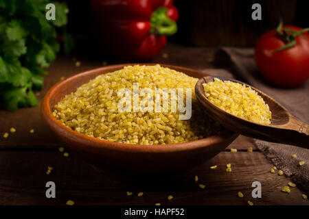 Raw bulgur, wheat grains in bowl on wooden table. Close up view Stock Photo