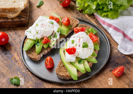 Close up view of delicious poached egg and avocado toasts garnished with chopped parsley. Selective focus Stock Photo