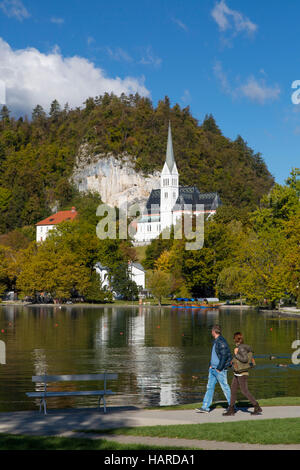 Couple walking around Lake Bled with St Martin's Parish Church beyond, Bled, Upper Carniola, Slovenia Stock Photo