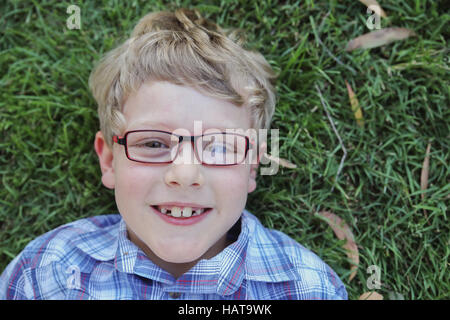 Happy little boy wearing glasses laying on grass Stock Photo