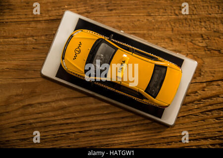 up view. yellow Taxi car - metal model stand on screen of white Smartphone. mobile phone lie on wooden table. empty copy space for inscription Stock Photo