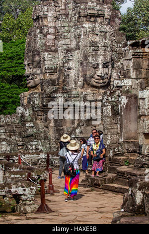 Ancient sandstone faces at Prasat Bayon in Angkor Thom stare down at tourists visiting the temple complex in Cambodia. Stock Photo