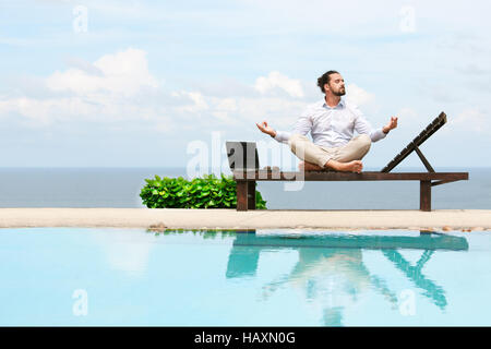 Businessman wearing a suit on deck chair doing Yoga on the beach Stock Photo