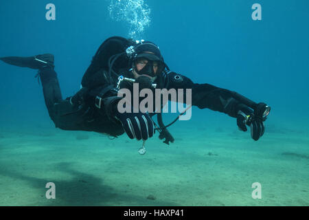 Professional scuba diver with black drysuit diving underwater in the ocean Stock Photo