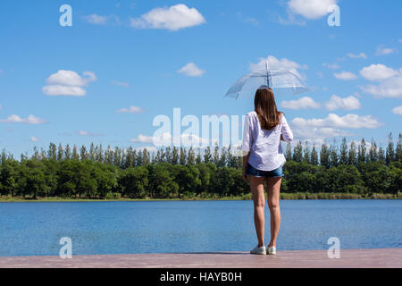 Woman holding an umbrella stand, a pond and watching nature. Stock Photo