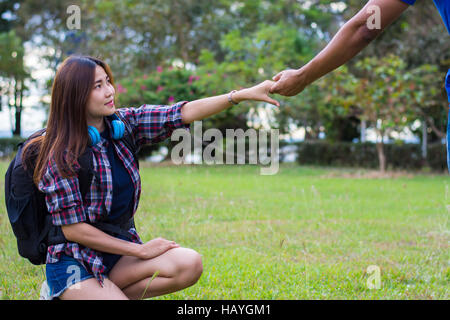 Woman sitting on the grass reaching to shake the hand of man. helping hand and love concept. Stock Photo