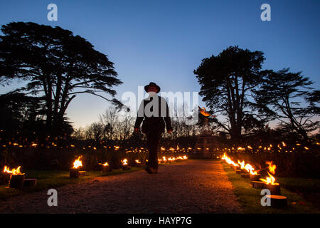 A male in silhouette agaisnt the darkeneing sky walks through the fire paths of the rose garden at Blenheim palace as the agrdens are lit up with festive lights for christmas. Stock Photo