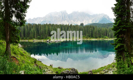 Lake Carezza - Karersee and the Latemar mountain in South Tyrol, Italy seen through fir trees. Stock Photo