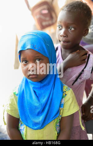 Diogue, Senegal-April 15, 2014: Couple of local girls leave the school for a while and get out to the street shyly but curiously to snoop around the Stock Photo