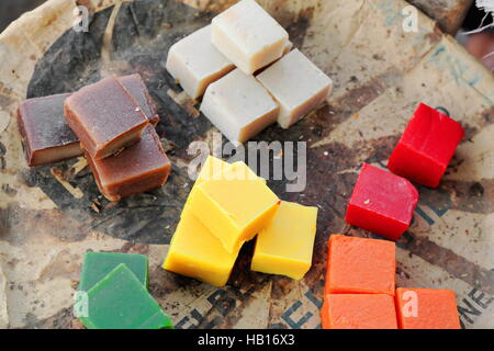 Quadrangular pieces of soap of various colors displayed on newsprint paper grouped by colors: brown-white-red-orange-yellow-green displayed for sale Stock Photo