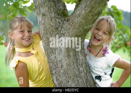 Two happy girls standing next to a tree trunk Stock Photo