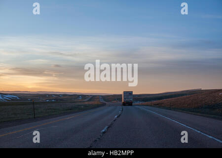 Highway drive toward a sunrise with a truck in the foreground on a winding road. Stock Photo