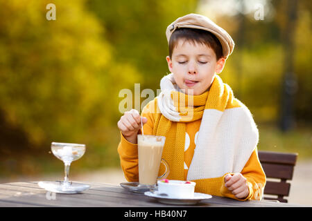 Cute little boy drinking hot chocolate in outdoor cafe on beautiful autumn day Stock Photo