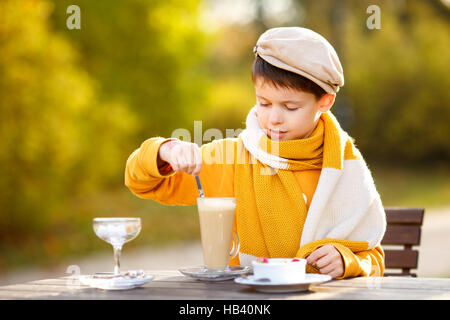 Cute little boy drinking hot chocolate in outdoor cafe on beautiful autumn day Stock Photo