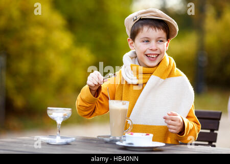 Cute little boy drinking hot chocolate in outdoor cafe on beautiful autumn day Stock Photo