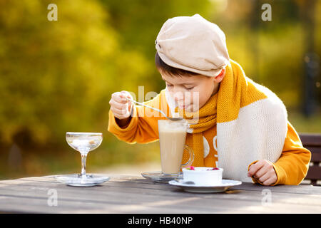 Cute little boy drinking hot chocolate in outdoor cafe on beautiful autumn day Stock Photo