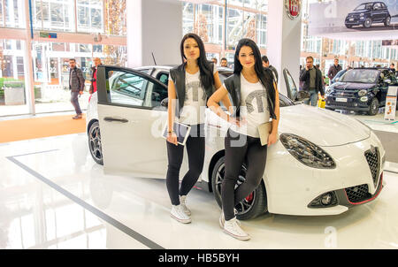 Bologna, Italy, Dec 03 2016 - two brunette models posing leaning to an white Alfa Romeo Giulietta car in the Fiat stand of the Motorshow 2016 in Bolog Stock Photo