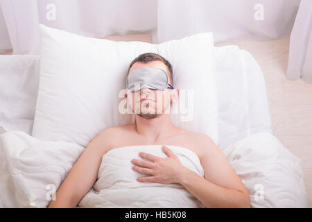 Sleeping young man in sleep mask on bed. Stock Photo