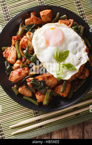 Stir-Fry Chicken with basil, green beans and a fried egg on a plate close-up. vertical view from above Stock Photo