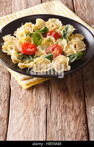 Delicious tortellini with spinach, tomatoes and cheese on a plate close-up. Vertical Stock Photo
