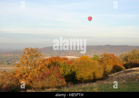 Chiltern Hills - autumn colours in the trees - cloud flecked blue sky - red hot air balloon gently floating over the hills Stock Photo