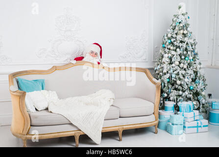 Santa Claus hiding behind a sofa over home interior Stock Photo