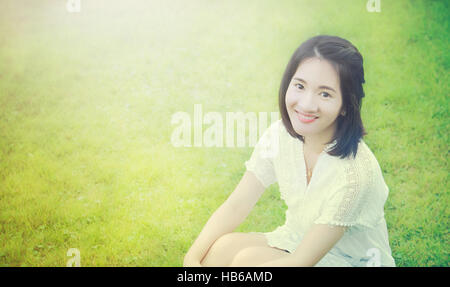 Portrait photo of Asian Thai young girl with smiley face in the garden with morning light and grass background and blank copy text space Stock Photo