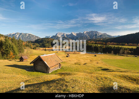 Haystack above Lake Gerold and the Karwendel mountains surrounded by colorful humpy meadows and autumn forest in afternoon sunlight, Bavaria, Germany Stock Photo