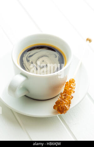 Brown amber sugar crystal on wooden stick and coffee cup on white table. Stock Photo