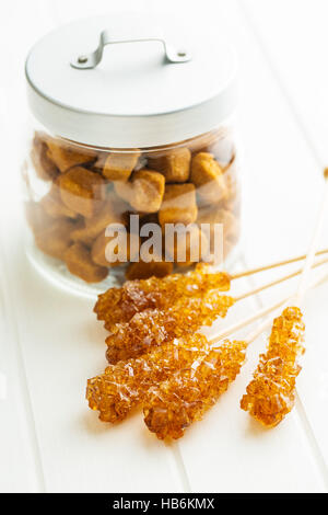 Brown amber sugar crystal on wooden stick and sugar cubes in jar. Stock Photo