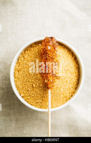 Brown amber sugar crystal on wooden stick and sugar crystals in bowl. Stock Photo
