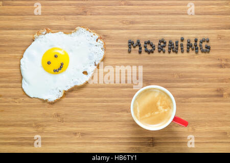 Smiling fried egg lying on a white plate and wooden cutting board with silver fork near it. Classic Breakfast concept. Stock Photo