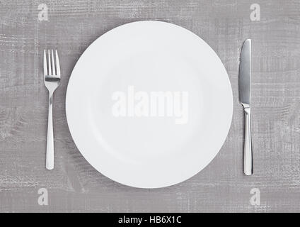 White round plate with fork and knife on wooden board background Stock Photo